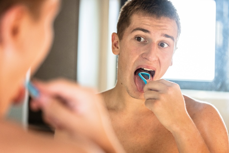 A young man is cleaning his tongue after a dentist consultation in St. Charles & Glen Ellyn, IL