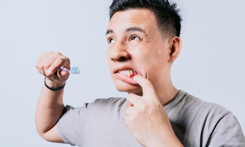 Person brushing teeth while checking bleeding gums in St. Charles and Glen Ellyn, IL