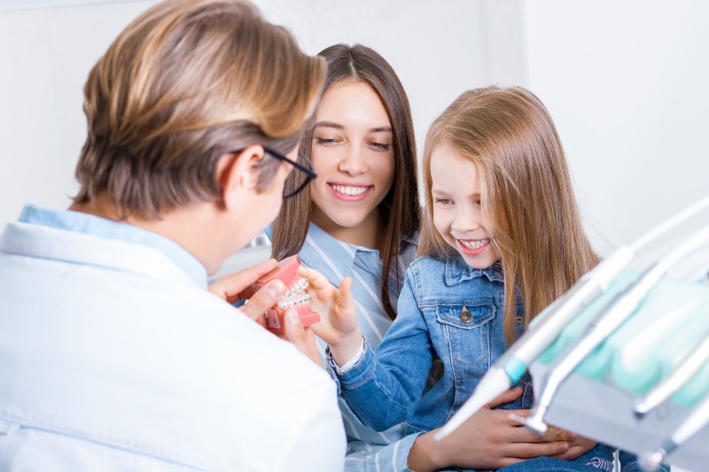 Orthodontist showing braces model to child with parent in St. Charles and Glen Ellyn, IL